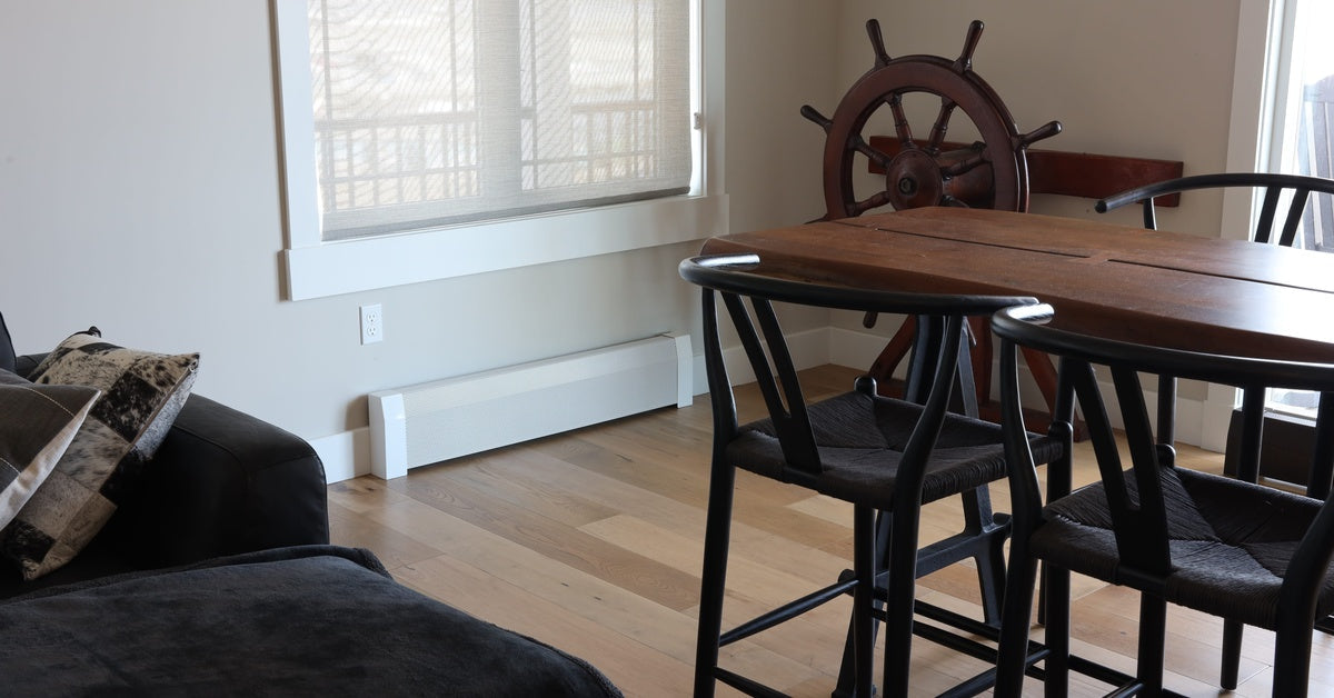 A baseboard heater with a white cover and endcaps on a wall in a dining room space with a table and chairs.