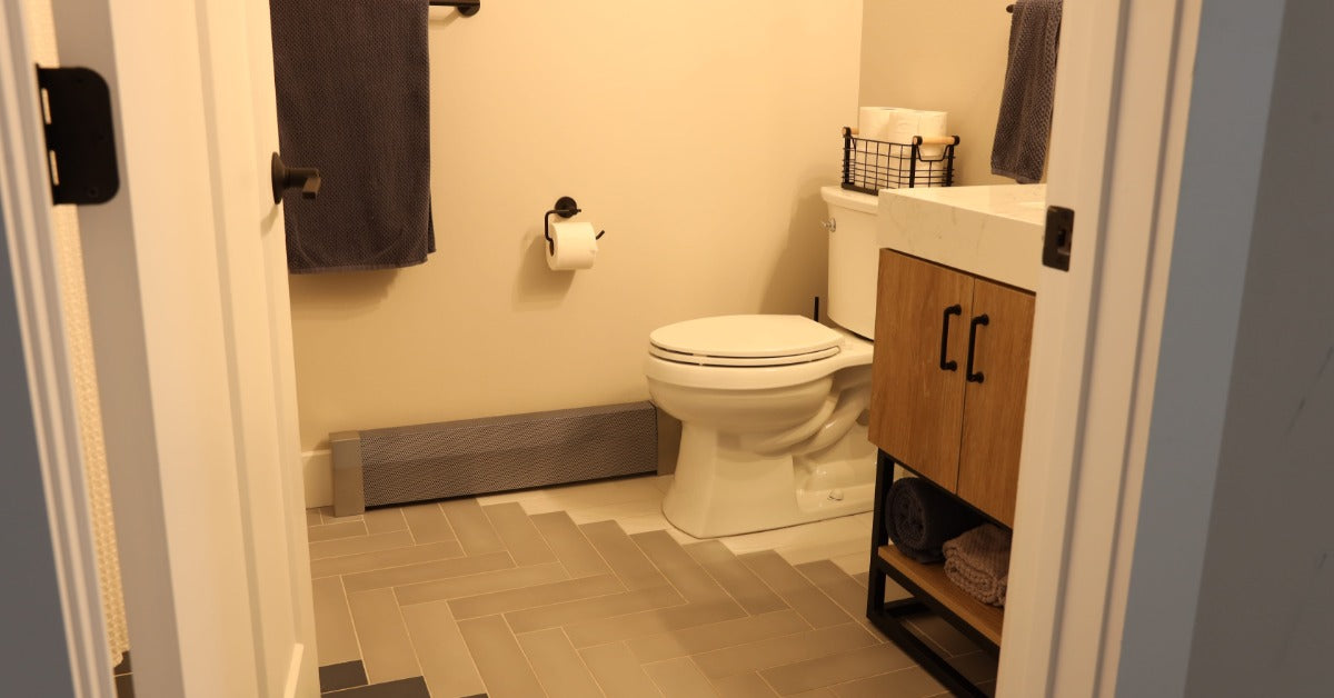 A modern bathroom space with herringbone tile on the floor and a baseboard heater along the far wall.