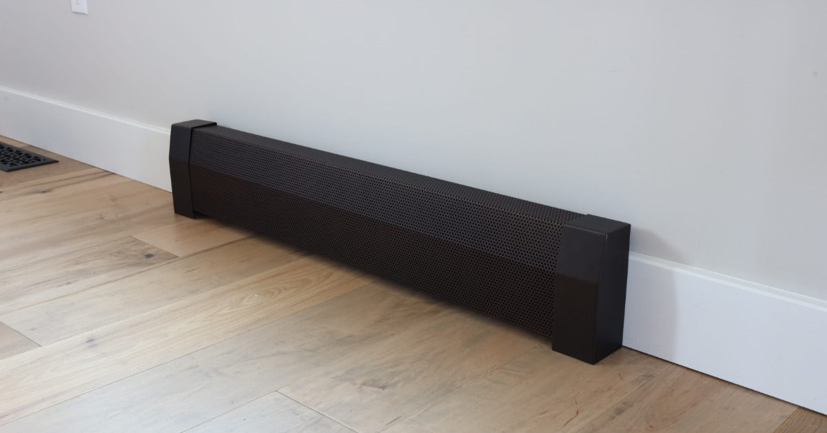 A close-up of a dark baseboard heater on a wall with white trim. There is an outlet on the wall near the heater.