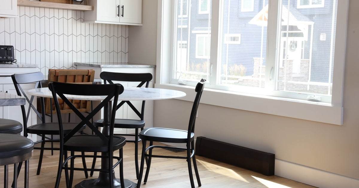 A dining room with a table and chairs, a large window, and a baseboard heater underneath the window.