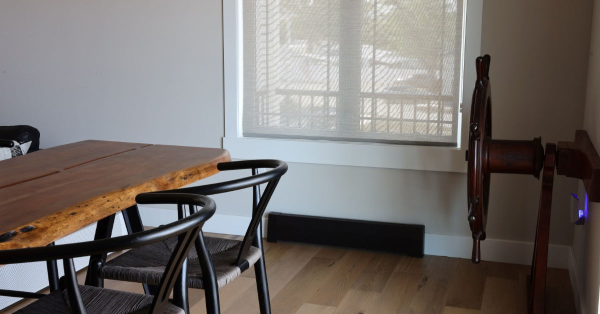 A modern dining area with a wooden table, black chairs, large window, baseboard heater, and a wooden ship wheel on the wall.