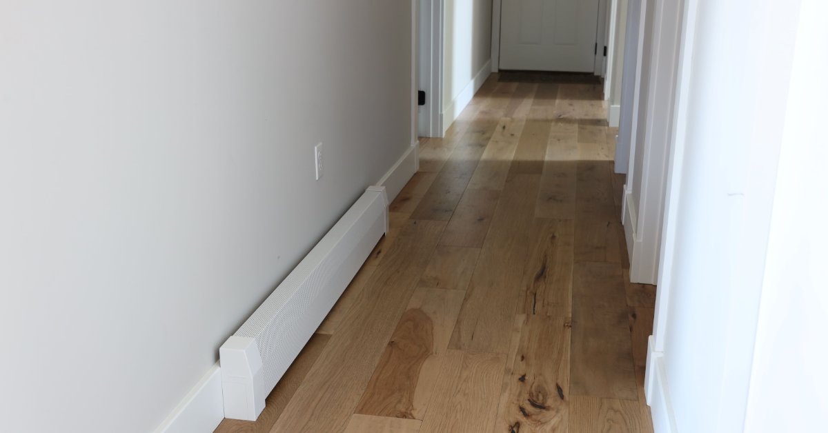 A bright hallway with hardwood flooring, white trim, multiple doorways, and a white baseboard heater cover.