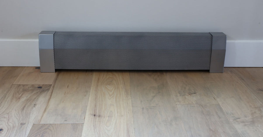 A long silver metal baseboard heater with a perforated front cover mounted along a wall above wood flooring.
