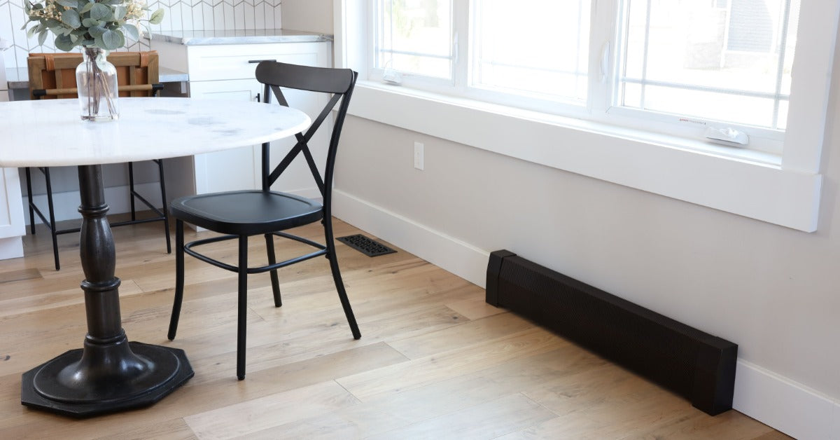 A bright dining area with a round table, black chair, large windows, and a black baseboard heater cover.