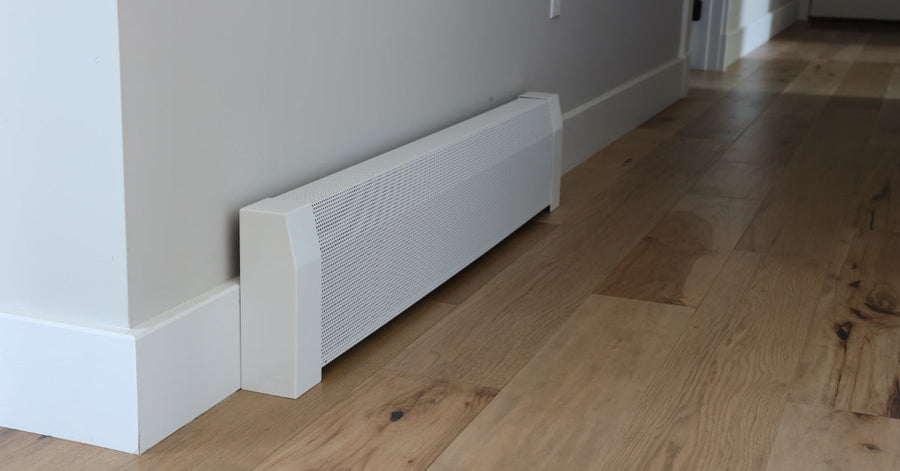 A white baseboard heater mounted along a light gray hallway wall above natural wood flooring and white trim.